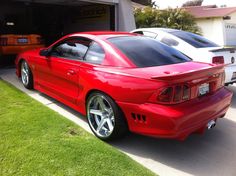 a red sports car parked in front of a garage with two other cars behind it