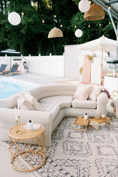 an outdoor living area with couches and tables next to a swimming pool in the background