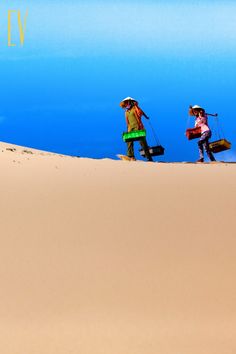 two people walking in the sand carrying luggage