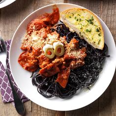 a white plate topped with pasta and meat covered in marinara sauce next to bread