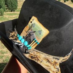 This is a unique western style hat with a custom band. The band is tan, white, black, and twine. It is embellished with turquoise stones, matches, and an armadillo playing card. Unique Hat Bands For Rodeo And Kentucky Derby, Artisan Turquoise Hats For Western-themed Events, Artisan Turquoise Hat For Western-themed Events, Handmade Western Hats For Kentucky Derby, Artisan Top Hat For Kentucky Derby And Western-themed Events, Handmade Western Costume Hats For Kentucky Derby, Handmade Hat Bands For Kentucky Derby, Artisan Hat Bands For Kentucky Derby Festival, Artisan Fedora Hat Bands For Western-themed Events