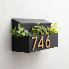 a black box with plants in it and the number 746 on it is attached to a white wall