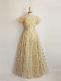 This gold silk and tulle gown would make a stunning alternative wedding dress or a decadent evening gown. The under layer is a luxurious pale gold silk dupion and the overlay is a featherlight art deco rose printed tulle. It can also be made in a shorter length for a 1950s vintage style dress.  It features a high necked version of our Bustier Grace bodice, with an illusion neckline and a keyhole opening at the back. The gently flared silhouette of the silk underlayer is then complemented by the Gold Vintage Dress, Gold Ball Gown With Fitted Bodice For Prom Season, Gold Ball Gown With Fitted Bodice For Prom, Fitted Gold Ball Gown For Debutante Ball, Gold Floor-length Ball Gown For Gala, Gold Ball Gown For Gala, Fitted Floor-length Gold Ball Gown, Gold Ball Gown Evening Dress With Fitted Bodice, Gold Ball Gown With Fitted Bodice