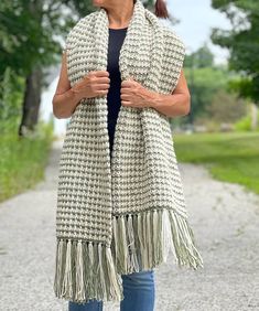 a woman standing on a dirt road wearing a white and black scarf with fringes