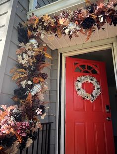 a red front door with a wreath on it and some leaves hanging from the side