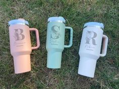 three different colored travel mugs sitting in the grass