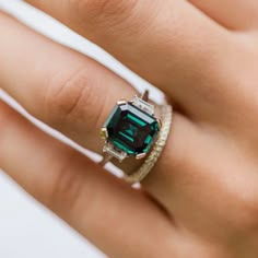 a woman's hand wearing a ring with an emerald and diamond set in it