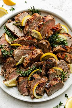 grilled steak with lemons and herbs on a white platter surrounded by sliced lemons