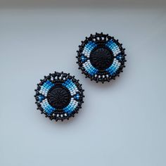 two blue and black beaded earrings sitting on top of a white table next to each other