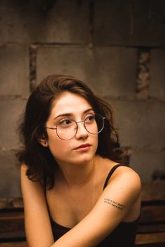 a woman wearing glasses sitting on top of a wooden bench next to a brick wall