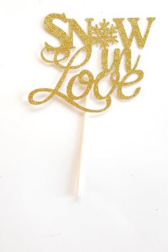 a cake topper with the words snow love on it in gold sparkles against a white background