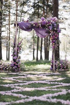 an outdoor ceremony with purple flowers and greenery on the ground, surrounded by trees