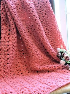 a pink crocheted blanket sitting on top of a chair next to a window