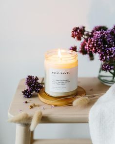 a candle sitting on top of a wooden table next to purple flowers and a white towel