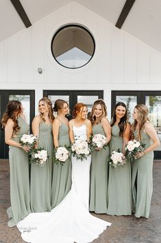 a group of women standing next to each other in front of a white building holding bouquets