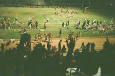 a group of people standing on top of a field next to a football field at night