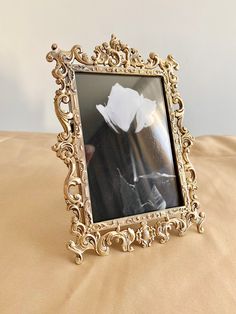 an ornate gold frame with a white flower in the center on a beige bed sheet