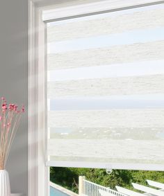 a vase with flowers in it next to a window that has blinds on the outside