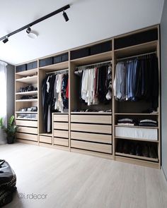 a walk in closet with lots of clothes on shelves and hanging lights above the doors