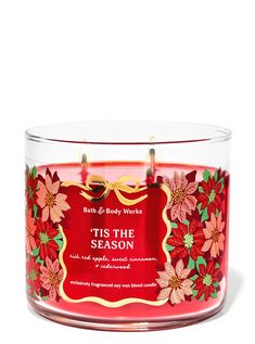 a red candle with poinsettis on it and a label that says tis the season