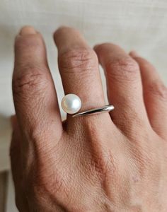 Add a touch of elegance and contemporary flair to your jewelry collection with the freshwater white pearl modern contempo ring. This striking open ring features one all natural freshwater button pearl with a smooth surface. The setting's modern contempo style is an open S925 sterling silver band that allows for an adjustable fit and a contemporary aesthetic. Open accommodates various finger sizes and adds a unique touch.  Pictures may reflect a close up view to ensure you have an accurate and de Modern White Pearl Ring As Gift, Modern White Pearl Ring For Anniversary, Modern White Pearl Ring Gift, Minimalist Sterling Silver Pearl Ring For Anniversary, White Minimalist Pearl Ring For Anniversary, Minimalist White Gold Ring With Pearl Drop, Minimalist White Gold Pearl Drop Ring, Minimalist White Pearl Ring For Anniversary, Modern Pearl Open Ring For Anniversary