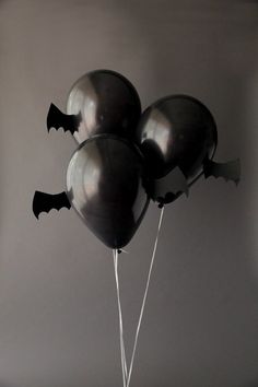 black balloons with bats attached to them are floating in the air against a gray background