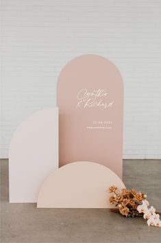 a pink and white wedding stationery with flowers on the ground in front of it