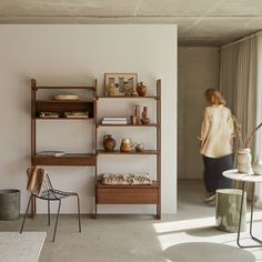 a woman standing in front of a shelf with vases and other items on it