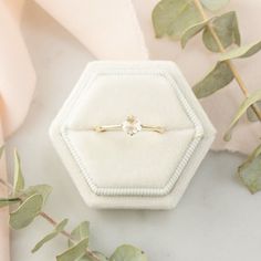 an engagement ring sitting on top of a white box next to eucalyptus leaves and pink flowers