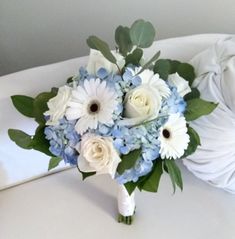 a bridal bouquet with white and blue flowers on a table next to a pillow