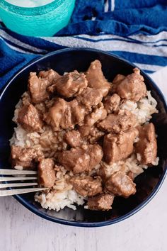 a bowl filled with meat and rice on top of a wooden table next to a blue towel