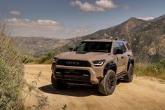 a toyota truck is driving on a dirt road in front of some mountains and bushes