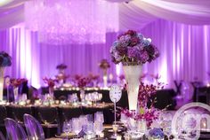 a tall vase filled with purple flowers sitting on top of a table covered in white linens