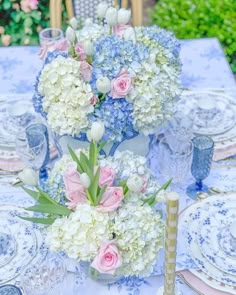 a blue and white table setting with pink and white flowers in vases on it