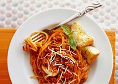 a white plate topped with spaghetti and meat covered in sauce next to bread on top of a table