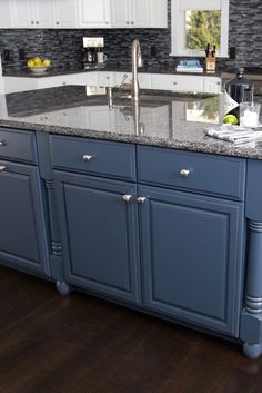 a kitchen with blue cabinets and granite counter tops on dark wood flooring in front of an island