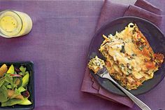 a plate of food and a bowl of salad on a purple table cloth with silverware