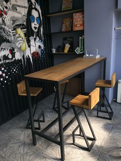 a wooden table with two stools next to it in front of a wall painting