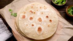 two flat breads sitting on top of a piece of wax paper next to bowls of lettuce