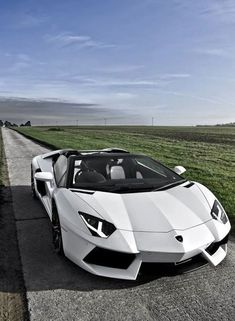 a white sports car parked on the side of a road next to an open field