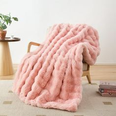 a pink blanket sitting on top of a wooden chair next to a potted plant