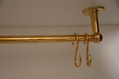 a close up of a gold colored curtain rod with two hooks on each end and a white wall in the background