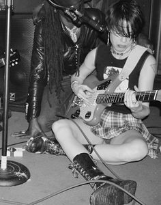 two people sitting on the floor with guitars in front of microphones and one person playing an electric guitar