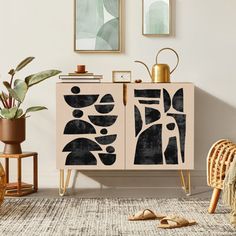 a cabinet with black and white designs on it in a living room next to some plants