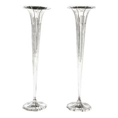 two tall silver vases sitting next to each other on top of a white surface