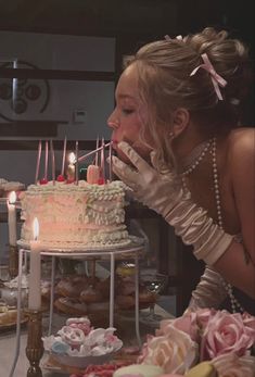 a woman blowing out candles on a cake with pink roses and other desserts in the background