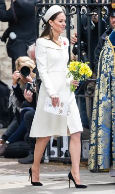 a woman in a white coat and hat walking past a man in a blue suit