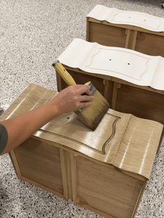 a person painting furniture with a paintbrush on the floor in front of two wooden boxes