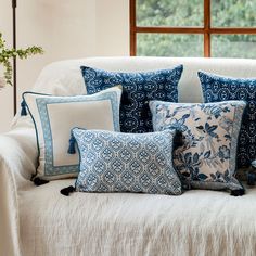 a white couch with blue and white pillows sitting on it's side in front of a window