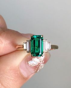 a woman's hand holding an emerald and diamond ring with three baguettes